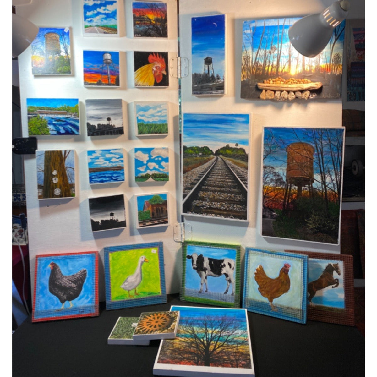 Collection of various paintings displayed on a wall and table.
